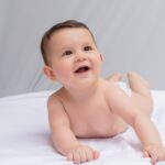 Adorable baby lying on a white sheet, smiling and looking happy.